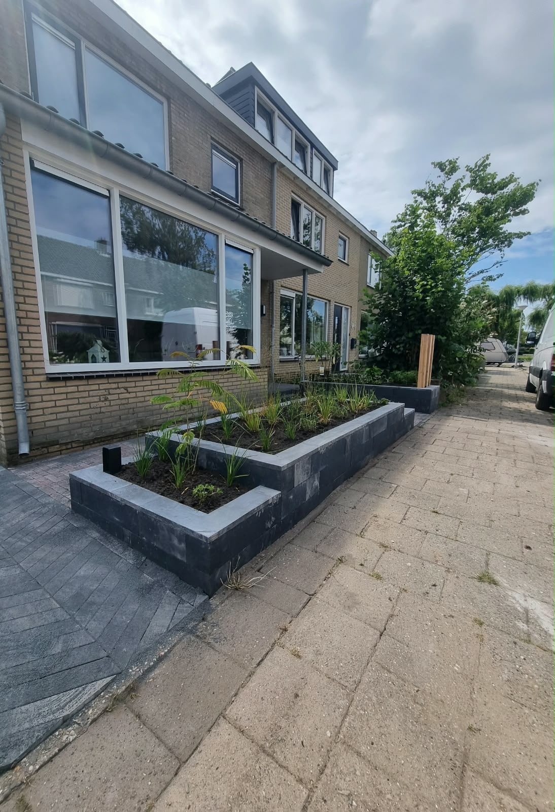 Voortuin met zwarte plantenbakken en gebakken klinkers